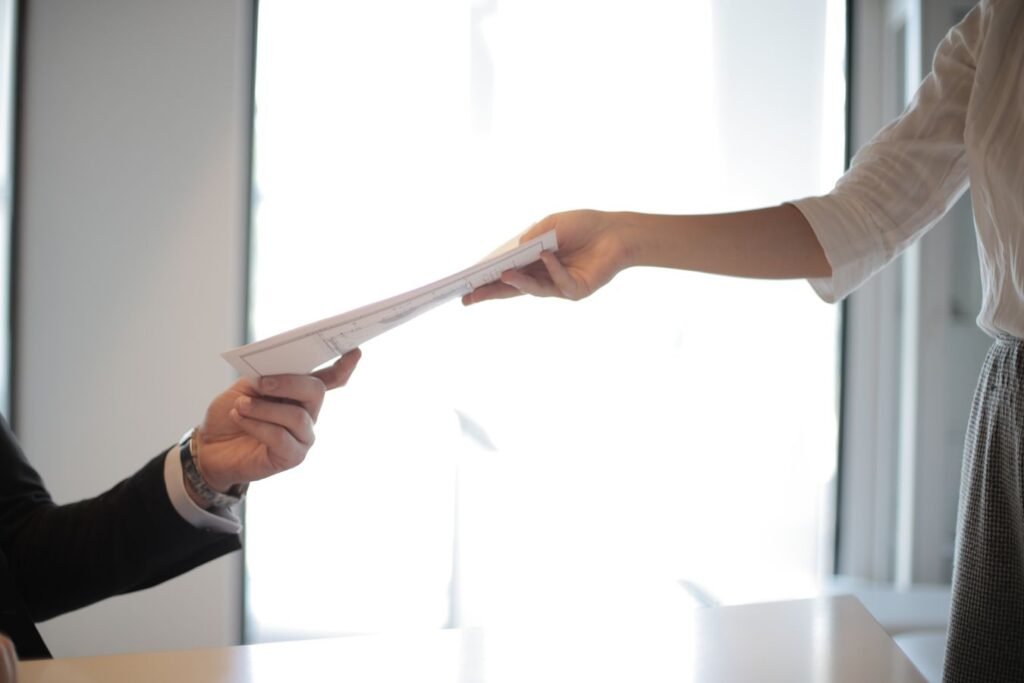 Close-up of hands exchanging documents in a business setting, representing ILOE unemployment insurance registration and claims