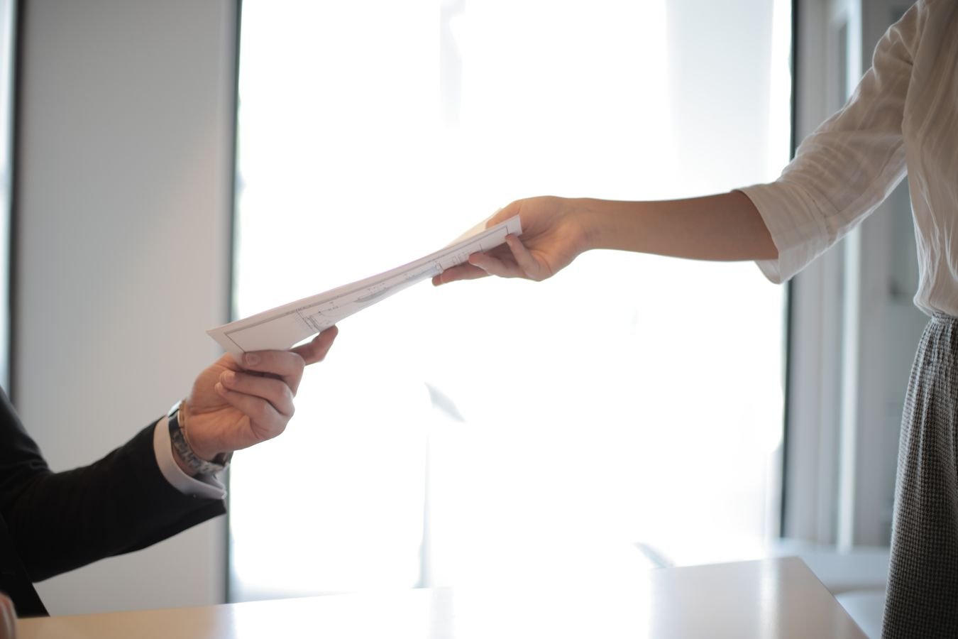 Close-up of hands exchanging documents in a business setting, representing ILOE unemployment insurance registration and claims