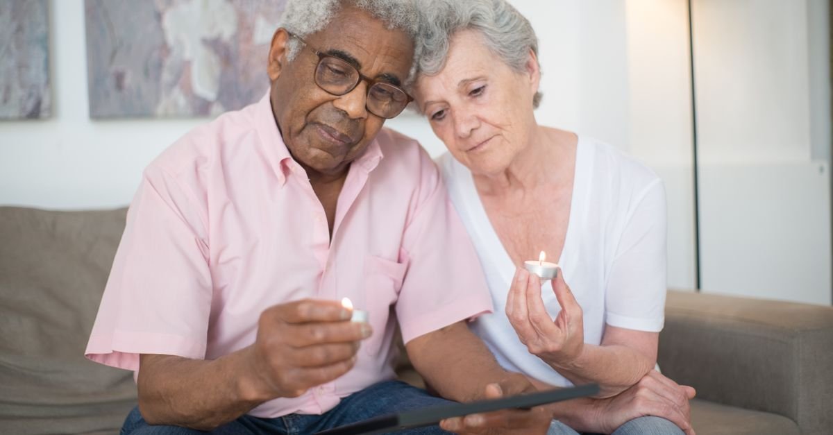 An elderly couple holding lit memorial candles together, representing the guide for expat families handling a death in the UAE