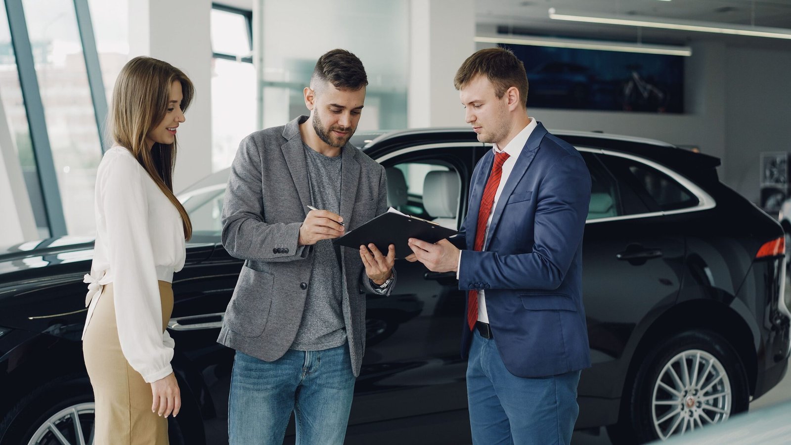Buyer and seller reviewing documents beside a car at a dealership, representing RTA vehicle ownership transfer in Dubai