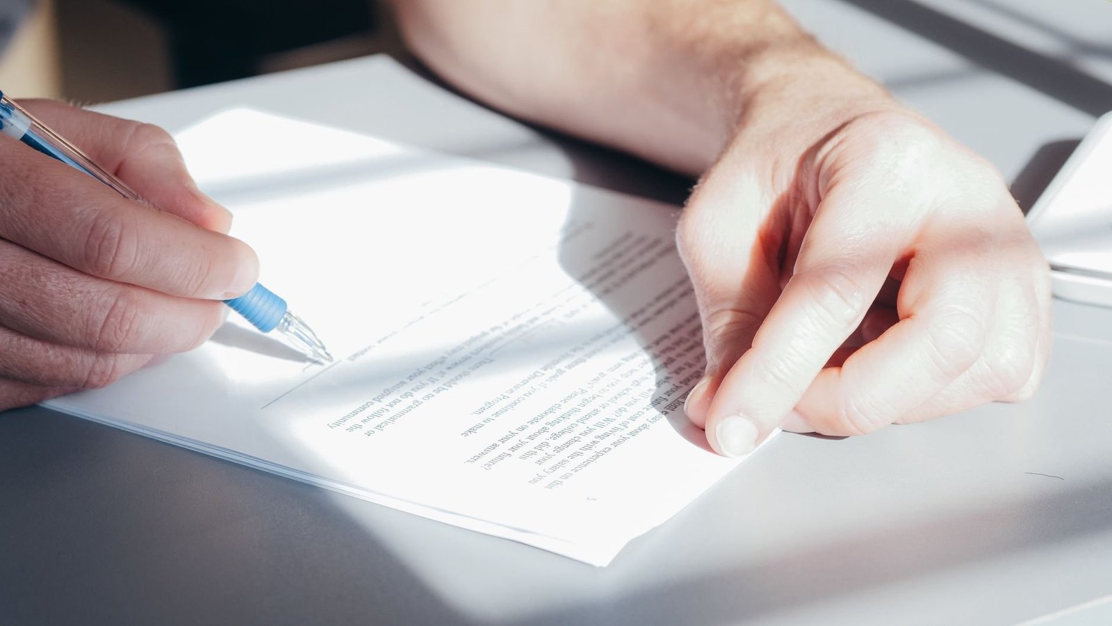 Hands signing a contract with a blue pen, representing a change to a UAE work permit and employment contract
