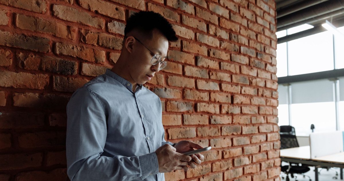 Man checking a job offer message on his smartphone in a brick-walled office, illustrating UAE job offer verification with MOHRE